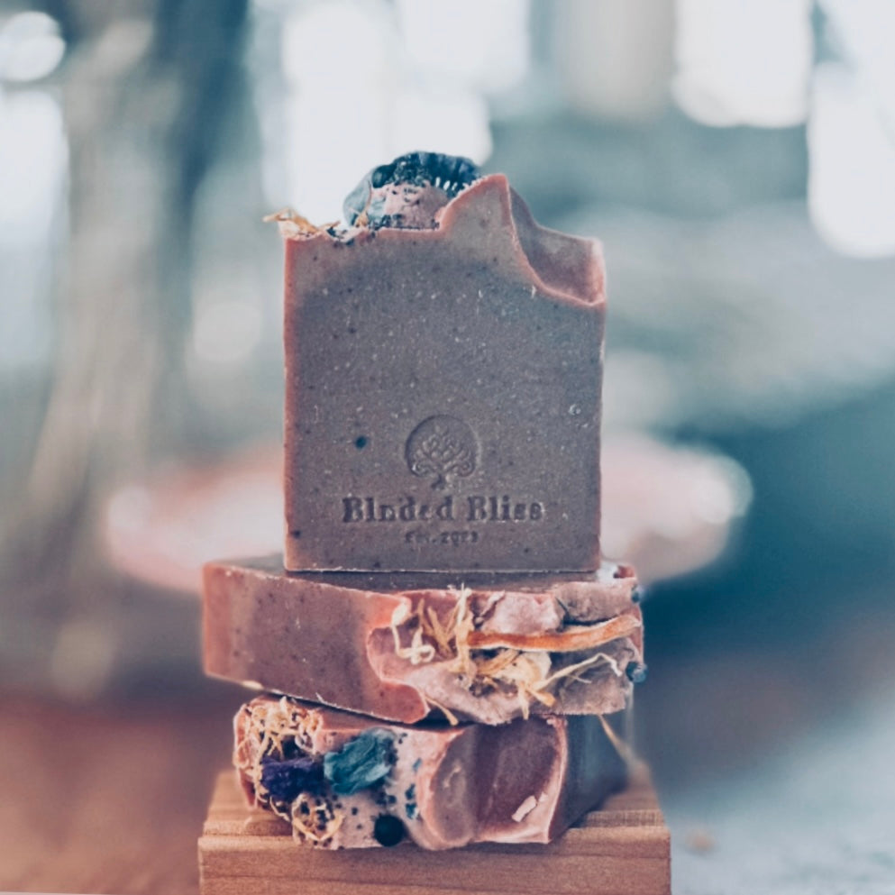 Golden Bloom Bar artisan soap by Blnded Bliss stacked on a wooden soap dish, featuring natural botanicals and embossed logo.