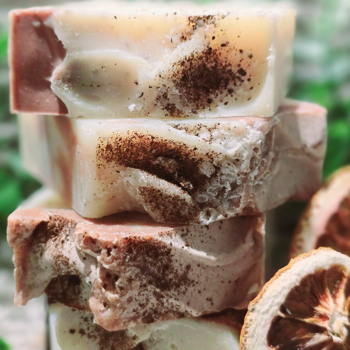 Close-up of Coconut Orange soap bars stacked, featuring creamy swirls, coconut shell powder topping, and dried orange slices