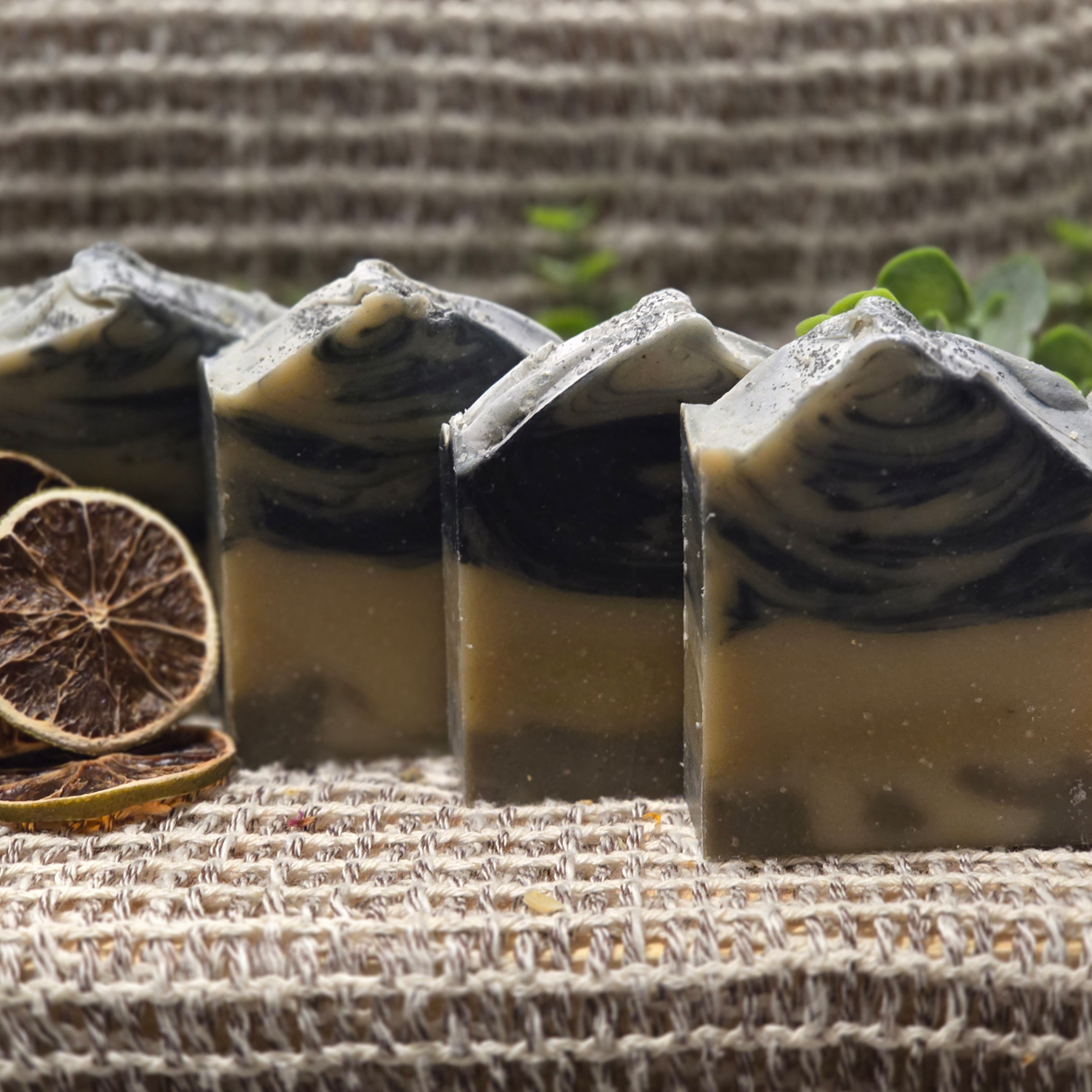 Four Lemon Patchouli soap bars with black and tan swirls, topped with volcanic salt, displayed with dried lime slices.