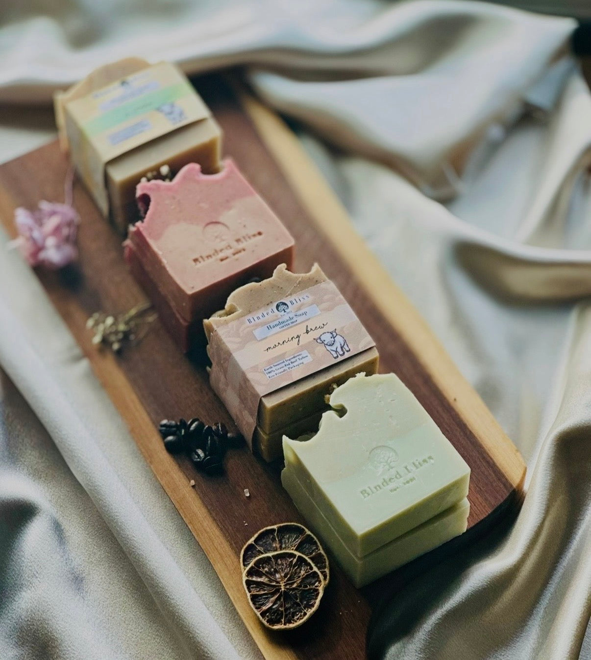 Four stacks of Blnded Bliss soaps on a cutting board with silk in the background