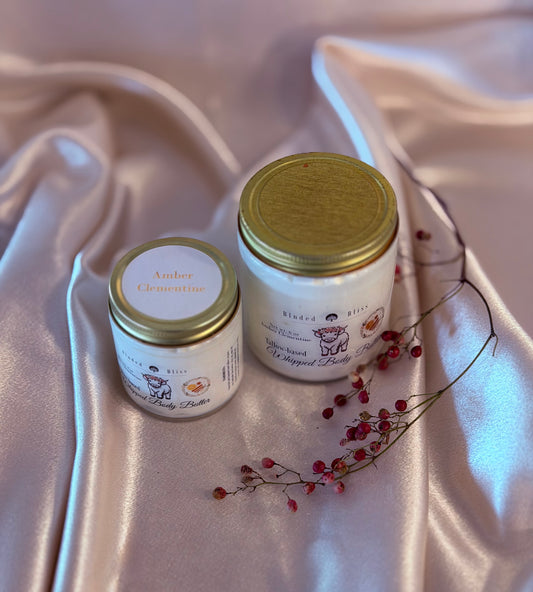 Two jars of body butter with gold lids on a satin surface.