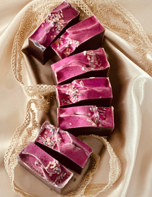 A luxurious set of handcrafted lavender soap bars with a rich purple swirl, topped with dried lavender buds, elegantly arranged on delicate lace fabric.