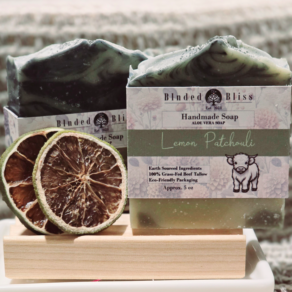 Lemon Patchouli handmade soap with deep green swirls, topped with black volcanic salt, displayed alongside dried lime slices on a wooden soap dish.