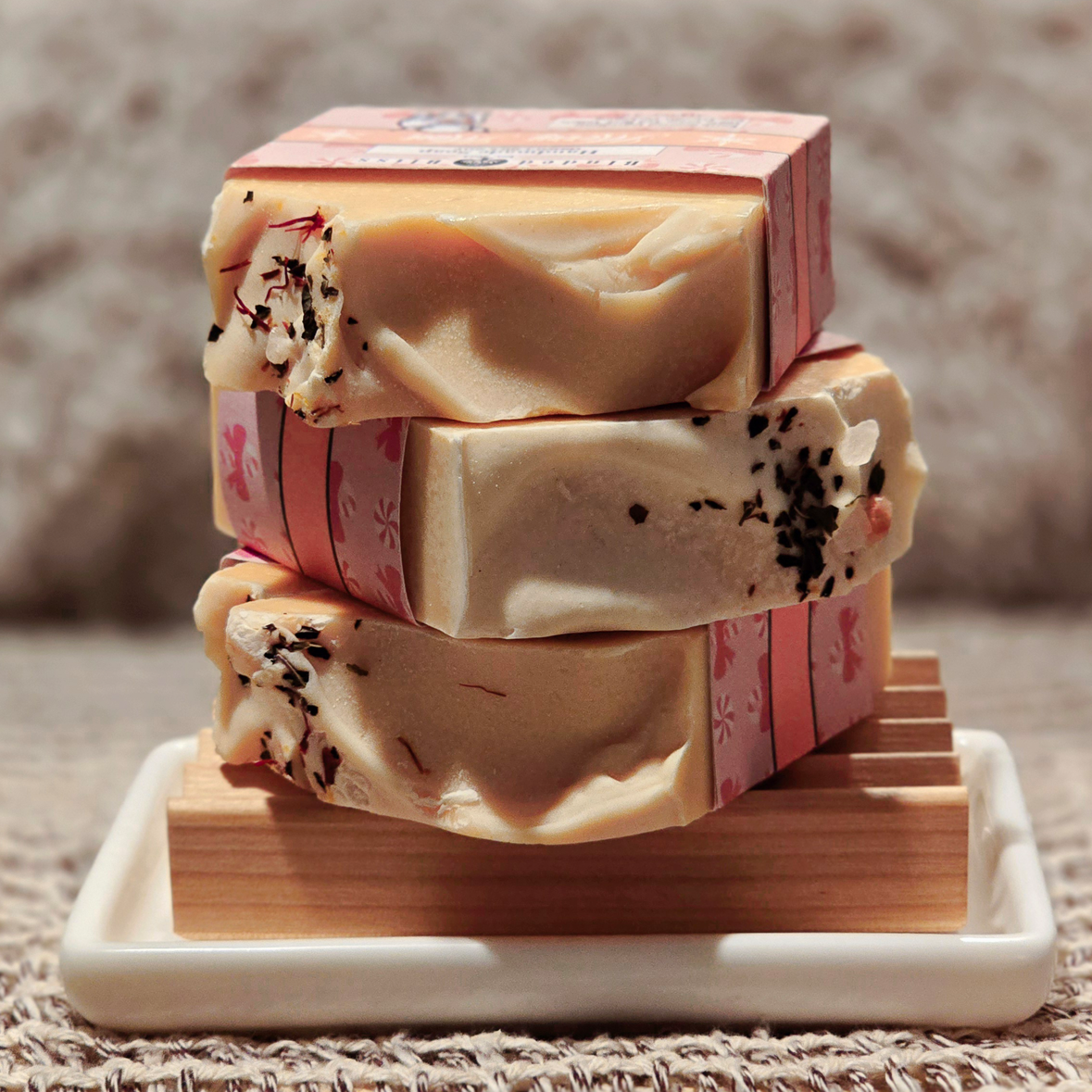 Stacked Merry Mint soap bars with creamy swirls, peppermint-inspired botanicals, and pink festive labels on a wooden soap dish.