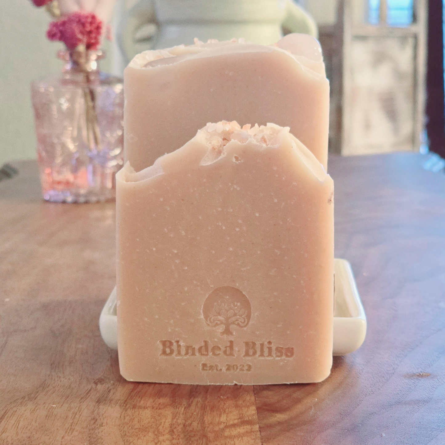 A frontal shot of a single Blush soap bar on a soap dish, emphasizing its artisanal design, creamy blush color, and embossed Blinded Bliss logo with "Est. 2023" engraving.